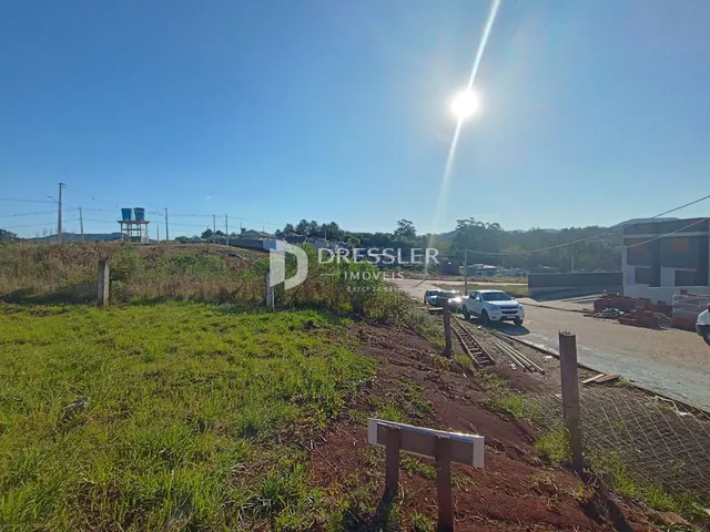 Vista externa de um terreno com vegetação e estruturas ao fundo.