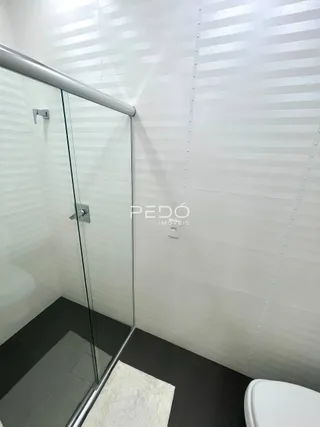 Interior de um banheiro com box de vidro e revestimento branco.