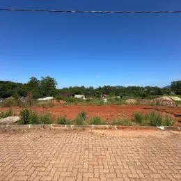 Área externa de terra vermelha com vegetação rasteira.