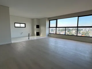 Sala ampla com piso claro e grande janela com vista da cidade.