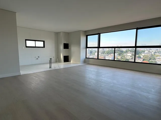 Sala ampla com piso claro e grande janela com vista da cidade.