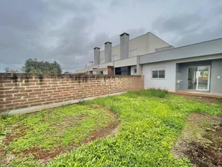 Vista externa da residência com muro de tijolos e jardim gramado.