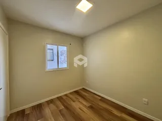 Uma sala interna com piso de madeira clara e paredes bege.