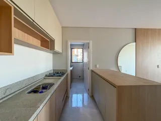 Vista da cozinha com armários de madeira clara e bancada de granito.