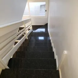 Corredor interno com revestimento branco e piso escuro.