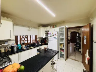 Vista interna de uma cozinha com armários brancos e bancada escura.