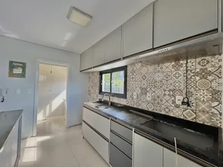 Vista da cozinha com armários brancos e revestimento cerâmico.