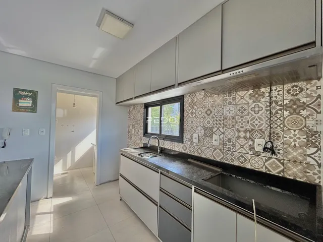 Vista da cozinha com armários brancos e revestimento cerâmico.