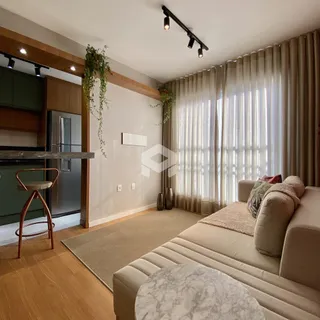Sala de estar com sofá e grandes janelas cobertas por cortinas claras.