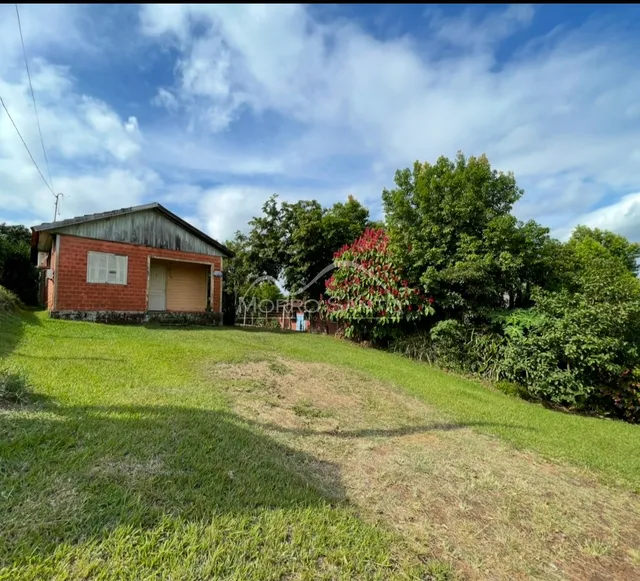 Vista externa de uma residência com terreno gramado e vegetação ao fundo.