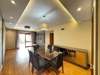 Sala de jantar com mesa de vidro e piso de madeira em um imóvel no Brasil.