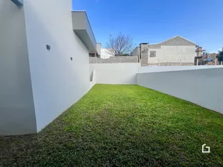 Vista externa de um quintal gramado cercado por um muro branco.