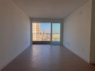 Uma sala ampla com piso de madeira e porta de vidro com vista para a cidade.