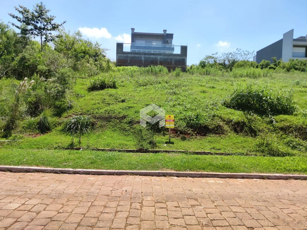 Vista externa de uma propriedade com grande área gramada e vegetação.