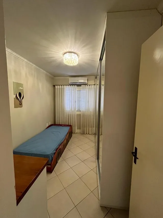 Um quarto com cama e janela coberta por cortinas brancas.