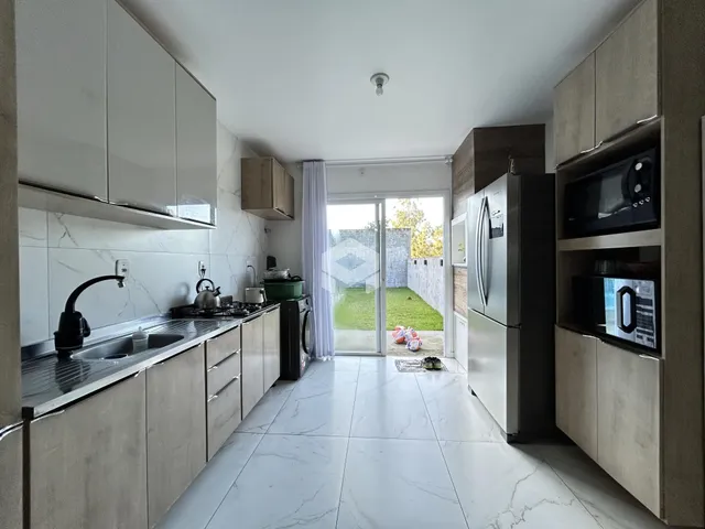 Cozinha moderna com armários brancos e piso de porcelanato, com vista para o jardim.
