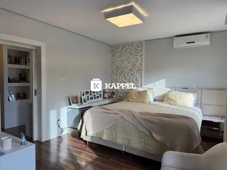 Quarto com cama grande e piso de madeira, apresentando um ambiente bem iluminado.