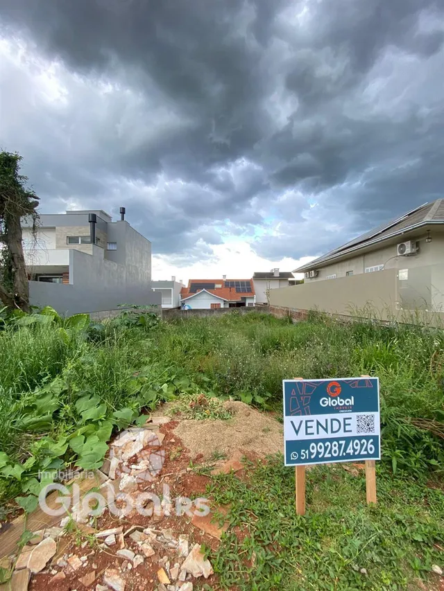 Vista externa de um terreno com vegetação densa e uma placa de venda no fundo.