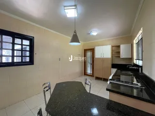 Interior de uma cozinha com armários brancos e bancada escura.