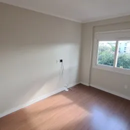 Vista interna de um cômodo com piso de madeira e parede branca.