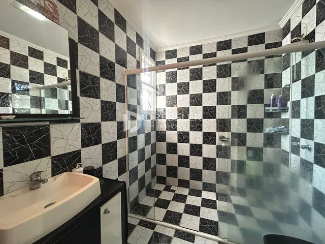Banheiro com revestimento de azulejos pretos e brancos e box de vidro.