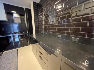 Detalhe da cozinha com revestimento de azulejos escuros e bancada reflexiva.