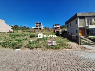 Vista externa de uma propriedade com vegetação seca e edifícios ao fundo sob um céu azul.
