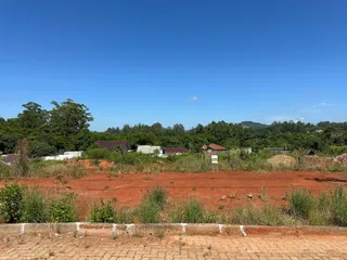 Paisagem de terra vermelha e vegetação rasteira sob um céu azul claro.