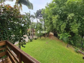 Vista externa de um jardim gramado cercado por árvores e cerca.