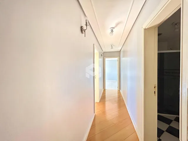 Corredor interno de uma residência com piso de madeira clara.