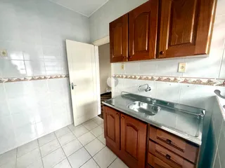 Interior de uma cozinha com armários de madeira e azulejos brancos.