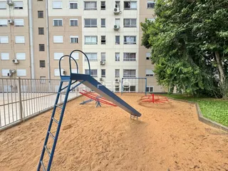 Área externa de lazer com playground e gramado de terra em Lajeado.