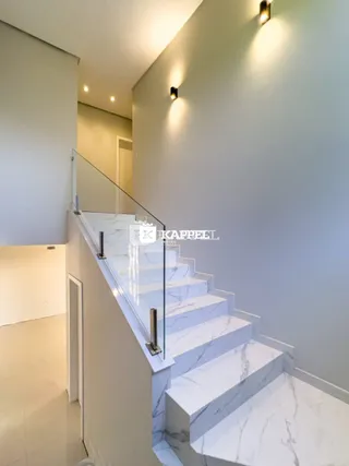 Escadaria de mármore branco com guarda-corpo de vidro em um corredor interno.