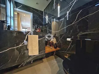 Detalhe do box e área molhada de um banheiro com revestimento em mármore escuro.