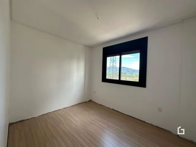 Ambiente interno de uma sala com piso de madeira clara e janela com vista para a paisagem.