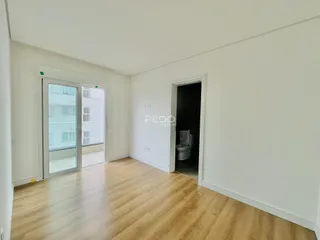 Vista interna de uma sala com piso de madeira clara e portas de acesso.