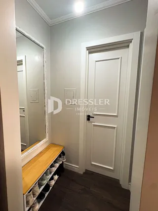 Hall de entrada com porta branca e espelho na parede de uma residência.