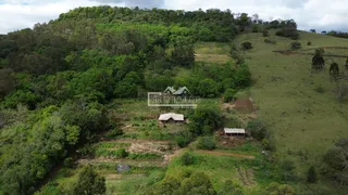Vista aérea de uma área de colinas com vegetação densa e algumas estruturas rurais.