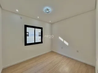 Ambiente interno de uma sala com piso de madeira clara e paredes brancas.