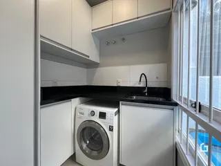 Vista de uma cozinha com armários brancos e máquina de lavar.