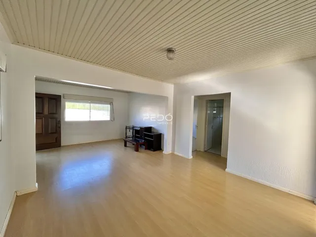 Uma sala ampla com piso de madeira clara e paredes brancas.
