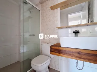 Banheiro com box de vidro e louças brancas.