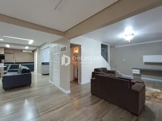 Sala de estar com piso de madeira clara e sofá marrom no interior de uma residência.
