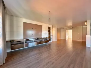 Interior de uma sala de estar moderna com piso de madeira clara e móveis embutidos.