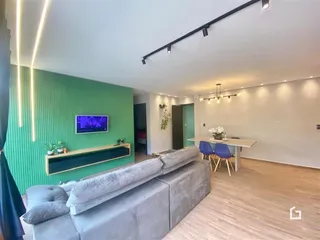 Sala de estar com sofá cinza e parede verde em um apartamento.
