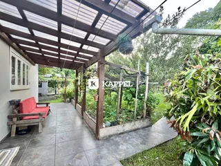 Patio coberto com piso de cerâmica e área verde ao ar livre em uma propriedade.