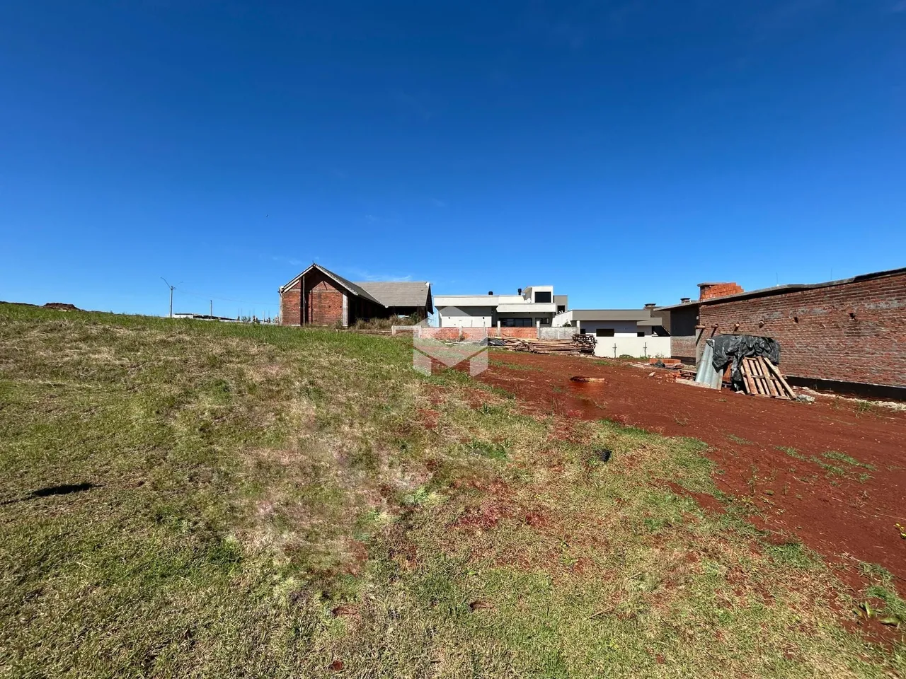 Vista externa de uma propriedade com terreno gramado e estruturas de alvenaria.