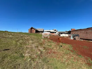 Vista externa de uma propriedade com terreno gramado e estruturas de alvenaria.