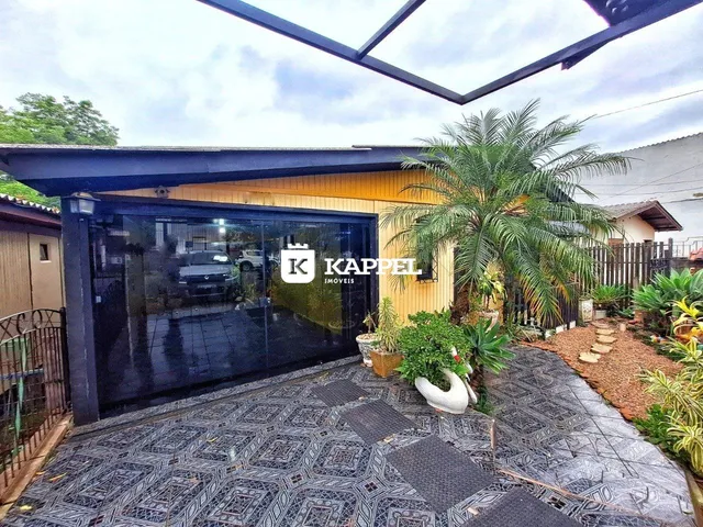Foto da fachada de uma residência com garagem e paisagismo tropical.