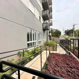 Vista da fachada de um prédio residencial com grade metálica e vegetação em Lajeado, Brasil.